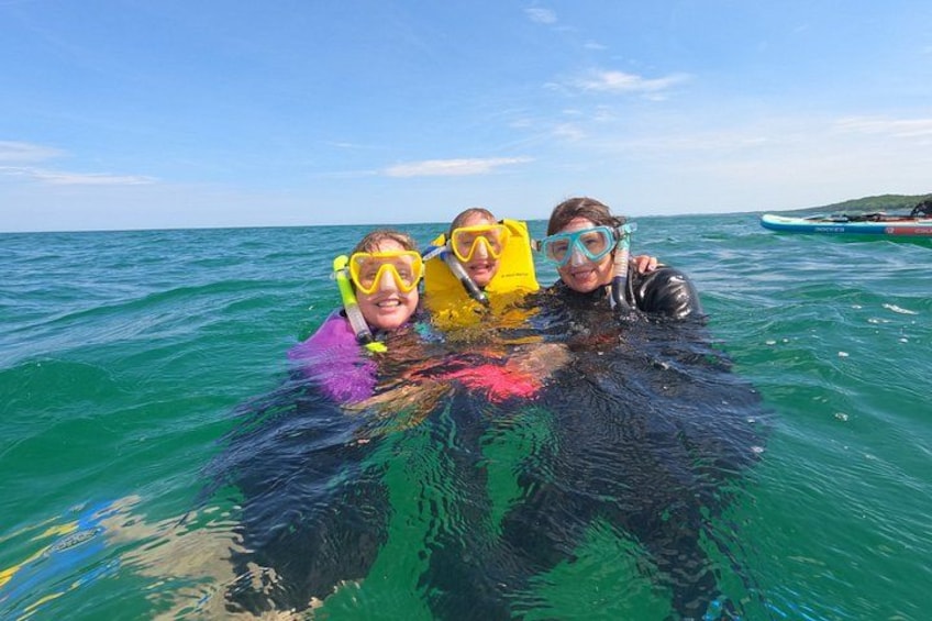Three people snorkeling in clear blue water with a boat in the background. 3