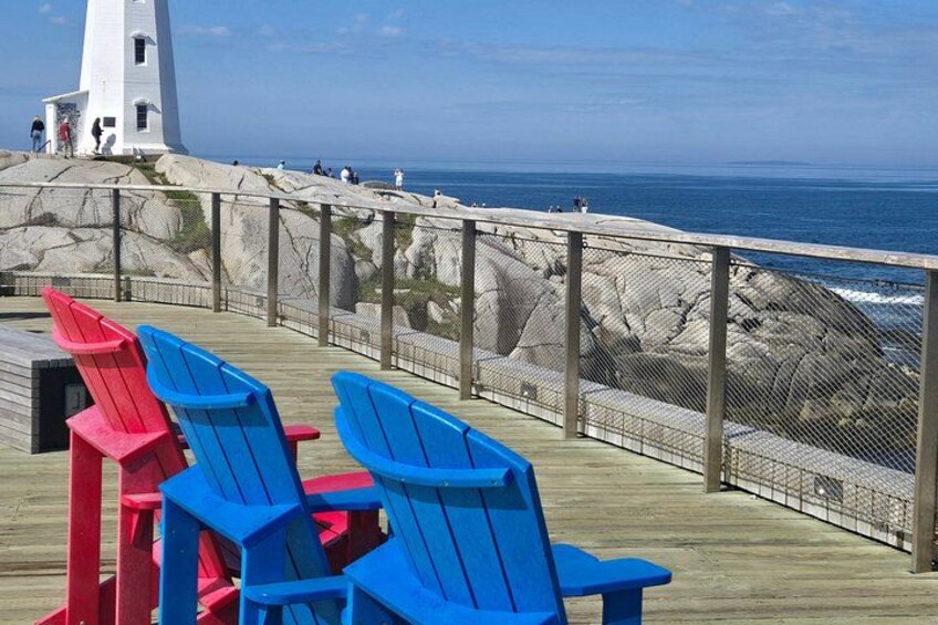 A lighthouse, a wooden deck, and chairs overlooking the ocean. 3