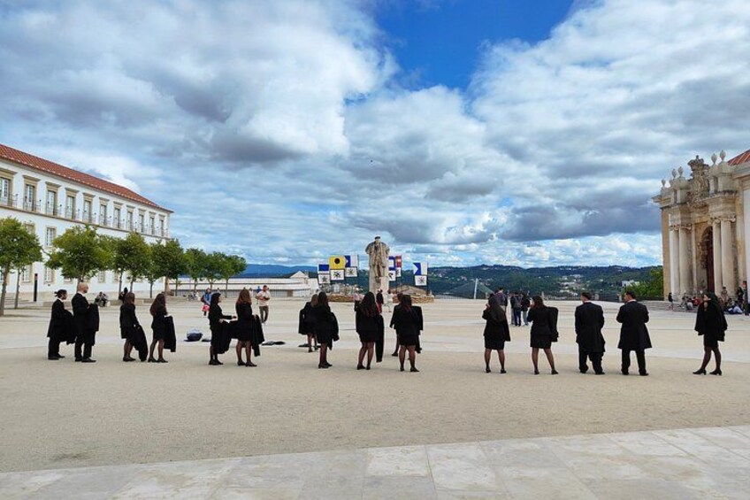 A group of people in formal attire standing in a plaza with buildings and a clear sky in the background. 2