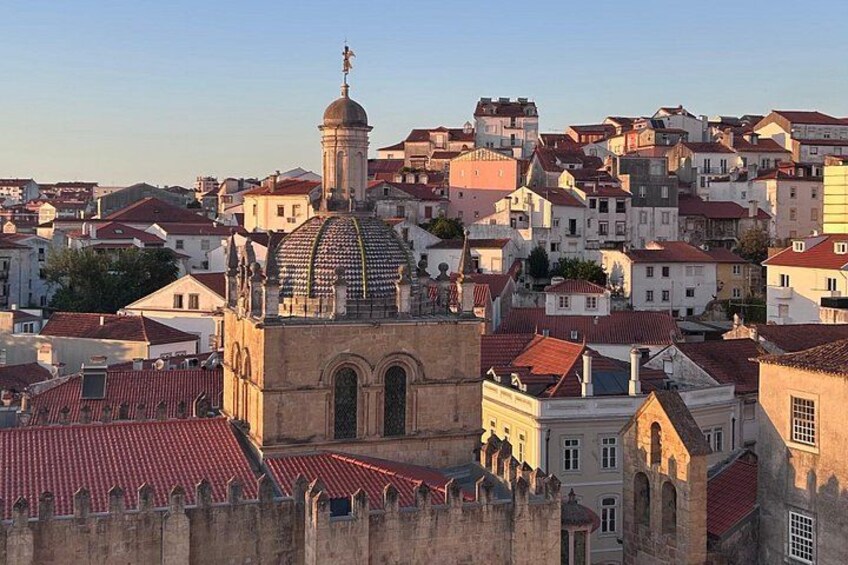 A historic cityscape with a prominent church featuring a dome and bell tower, surrounded by densely packed buildings with red-tiled roofs. 3