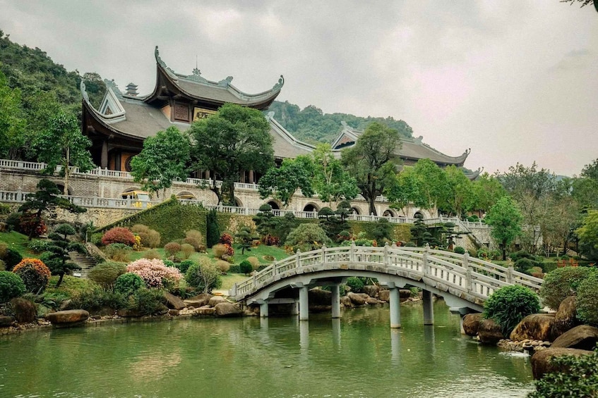 A traditional Chinese building with a curved bridge over a pond, surrounded by landscaped gardens and trees. 4