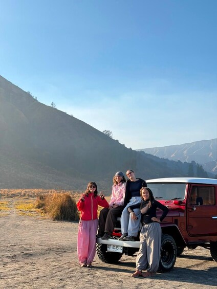 A group of people sitting on a red vehicle in a natural landscape with mountains in the background. 2
