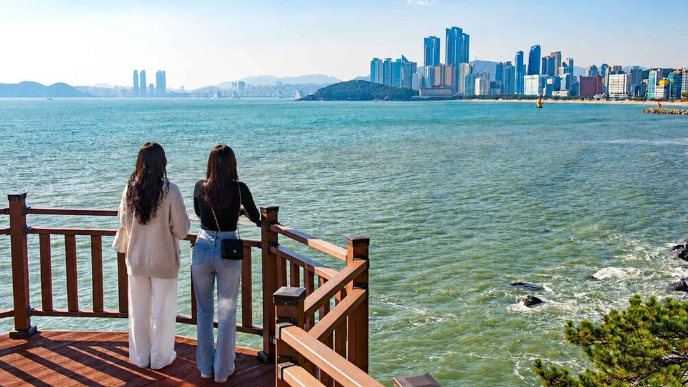 Two people on a wooden deck overlooking a body of water with a city skyline in the background. 4
