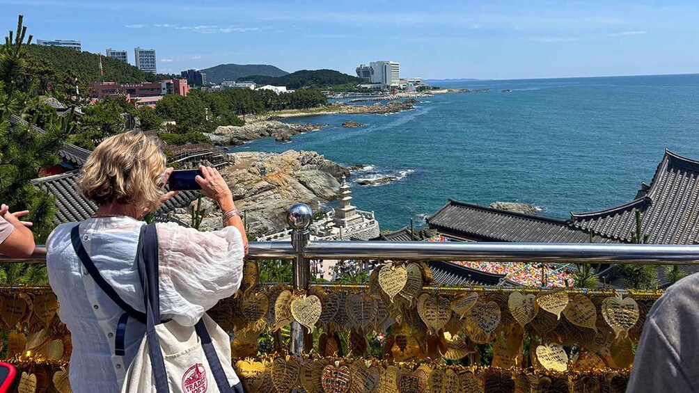A person taking a photo of a coastal landscape with traditional buildings and a rocky shoreline. 4