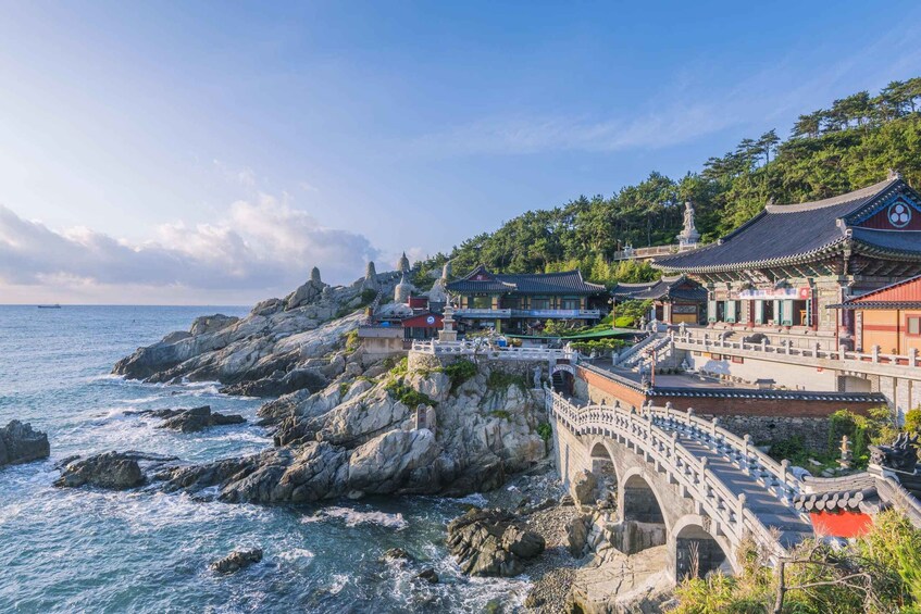 A coastal temple complex with traditional architecture, a stone bridge, and rocky cliffs. 3