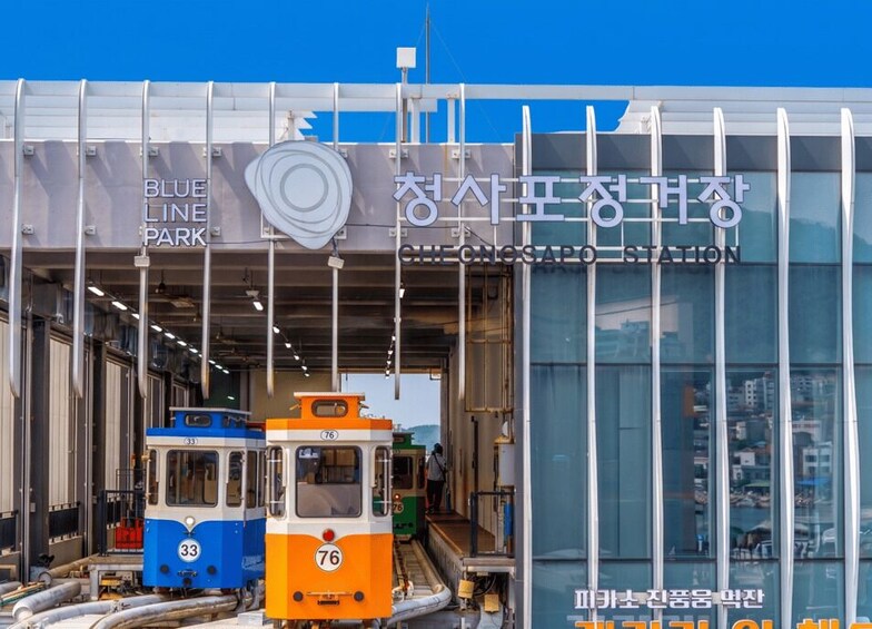 A train station with two trains, one blue and one orange, and a building with signage in both Korean and English. 2
