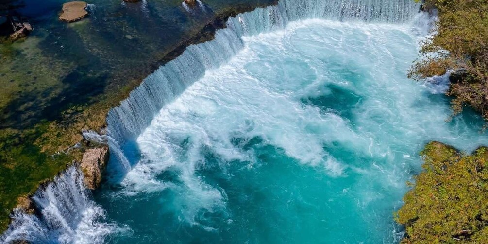 A waterfall cascading over rocks into a turquoise pool surrounded by greenery. 2