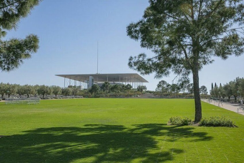 A modern building with a flat roof, surrounded by a well-maintained grassy field and trees. 1