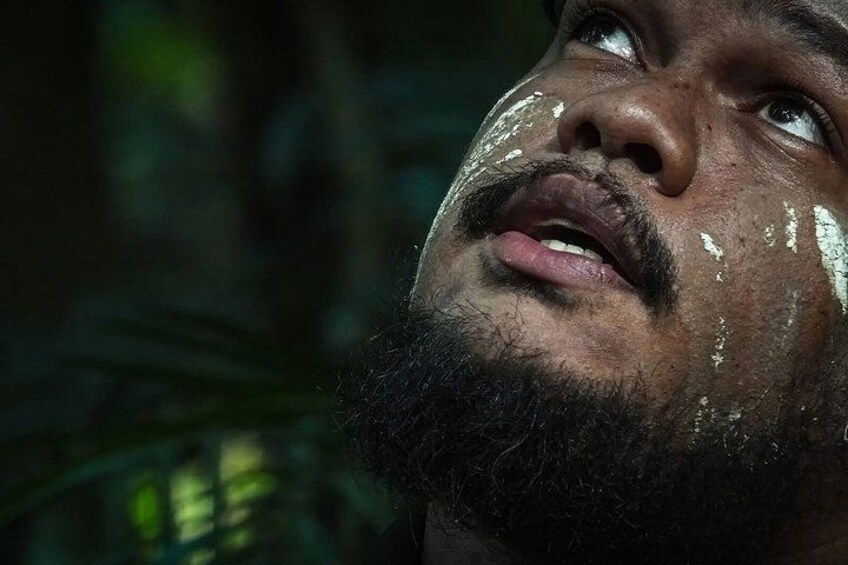 A person with a blurred face, wearing a dark jacket, and a background of dense foliage. 3