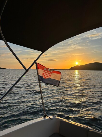A boat with a Croatian flag, a sunset over water, and distant land. 1