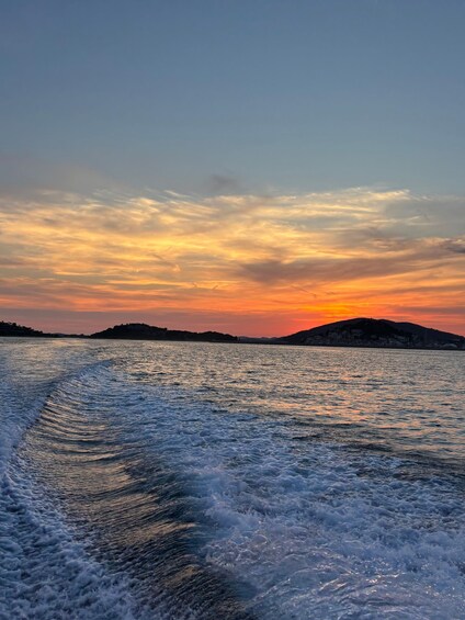 A body of water with waves, a sunset, and distant landforms. 2