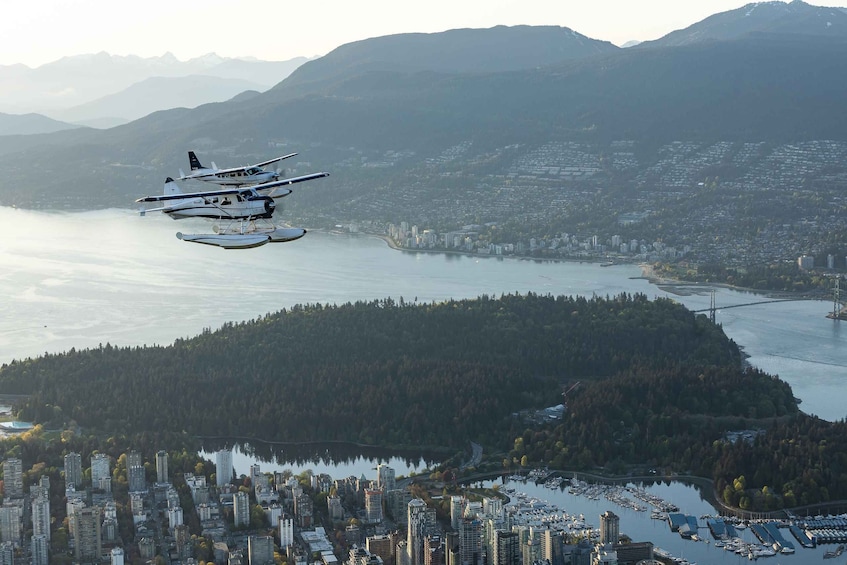A seaplane flying over a coastal city with a dense urban area and a forested island. 1