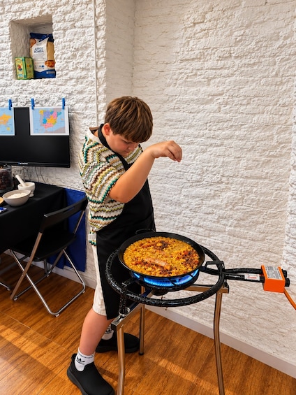A child cooking on a portable stove with a pan of food. 5