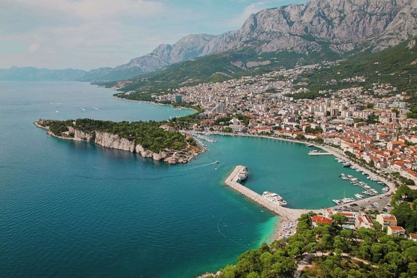 A coastal town with a marina, a peninsula with cliffs, and mountainous terrain in the background. 1