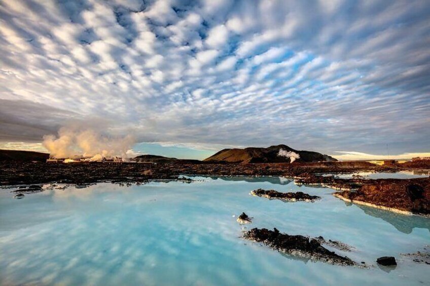 A geothermal pool with steam rising, surrounded by mountains and a cloudy sky. 2