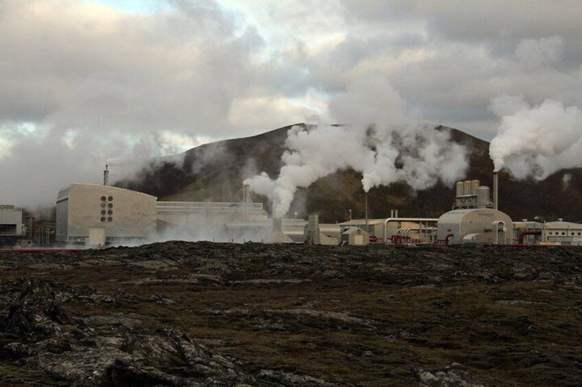A geothermal power plant with steam emissions, industrial buildings, and a mountainous backdrop. 5