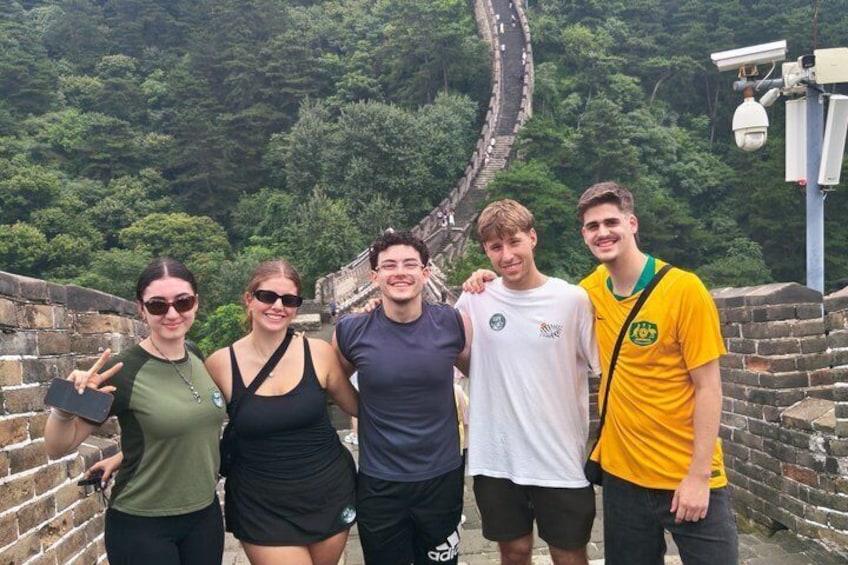 A group of people standing on a wall with a historic wall and lush greenery in the background. 1
