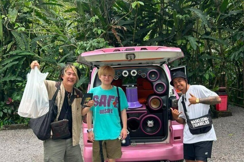 Three people standing in front of a pink vehicle with a speaker-filled trunk. 4
