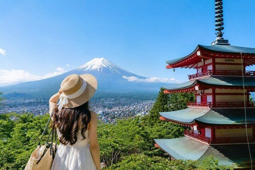 A person in a white dress and straw hat overlooking a traditional Japanese pagoda and Mount Fuji in the distance. 3