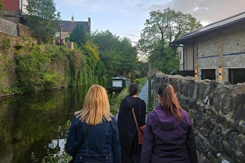 A canal with buildings on either side, a stone wall, and a person in a purple jacket. 2