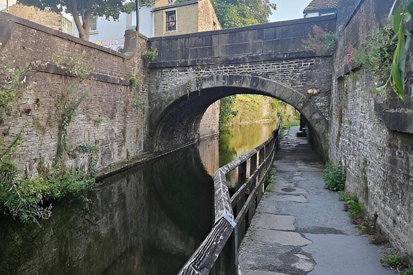 An old stone bridge over a narrow canal with a paved walkway alongside. 2