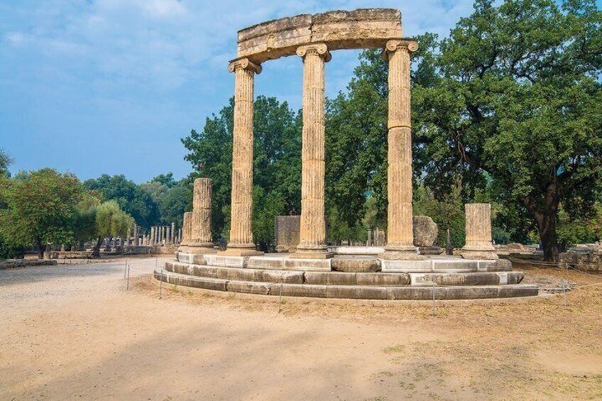 Ancient columns with a circular base, surrounded by trees and open space. 3