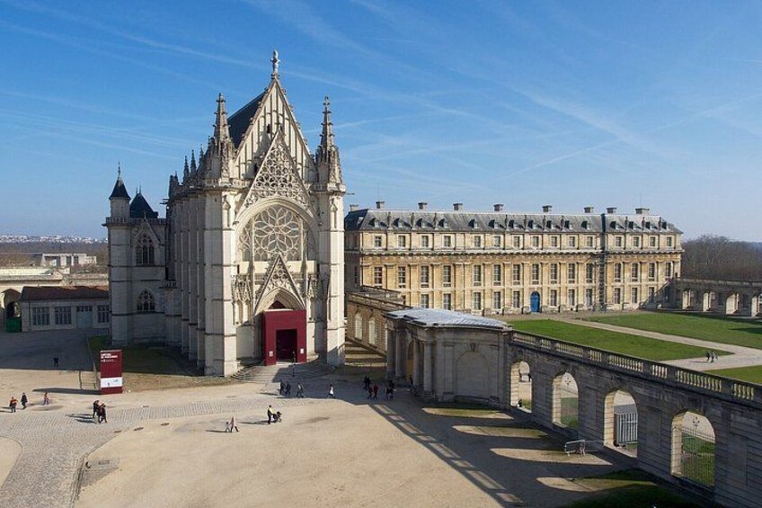 A large historic building with a prominent entrance, a long covered walkway, and a bridge connecting to another structure. 5