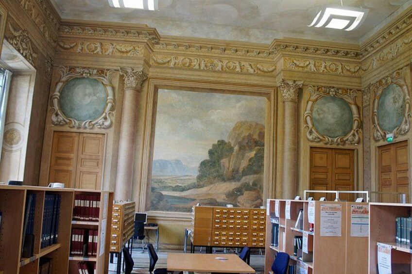 A library interior with ornate columns, a large mural, and bookshelves. 3