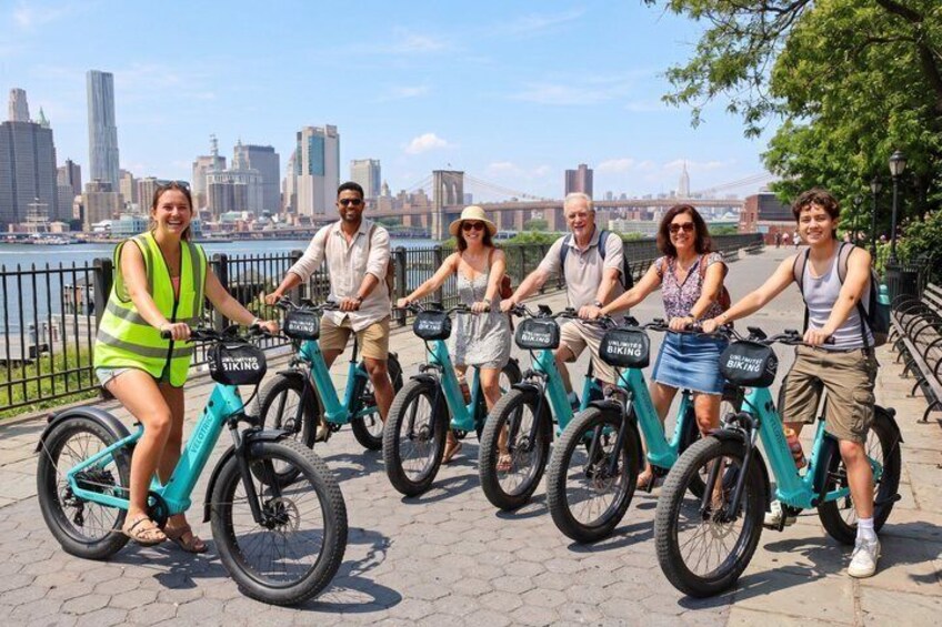 A group of people riding electric bikes on a waterfront promenade with a city skyline in the background. 5