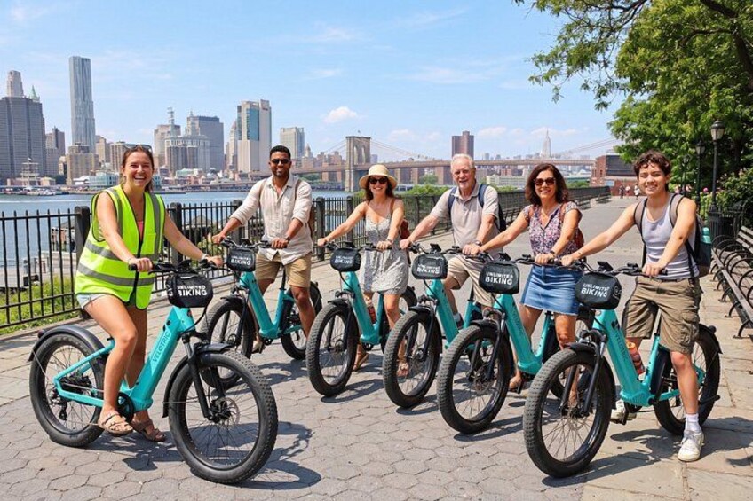 A group of people riding electric bikes along a waterfront promenade with a city skyline in the background. 5