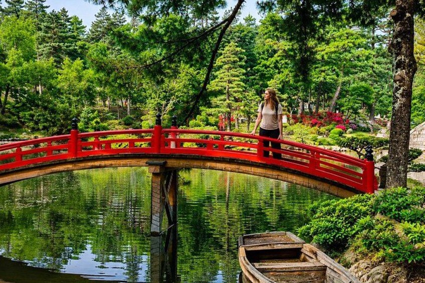 A red bridge over a pond, surrounded by lush greenery and trees. 3