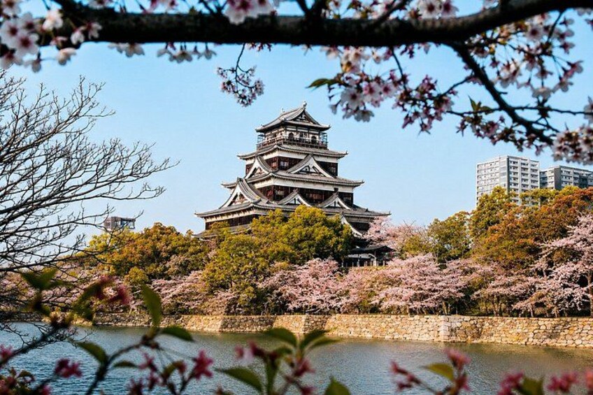 A traditional Japanese castle with cherry blossoms in the foreground and a river in the background. 4