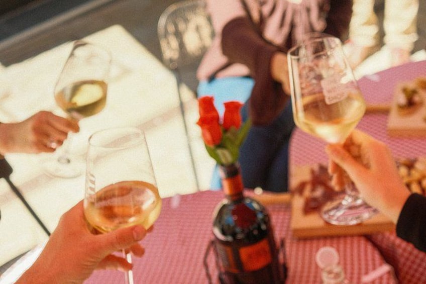 People toasting with wine glasses, a bottle of wine, and red roses on a table. 3