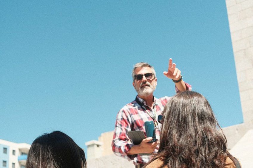 A person speaking to an audience outdoors with buildings in the background. 5