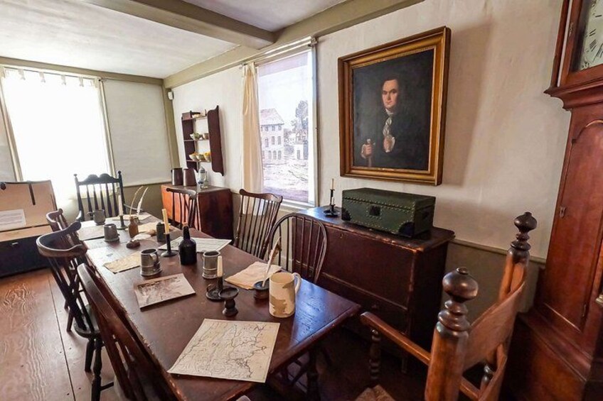 A dining room with a wooden table, chairs, a painting, a clock, and a window with curtains. 4