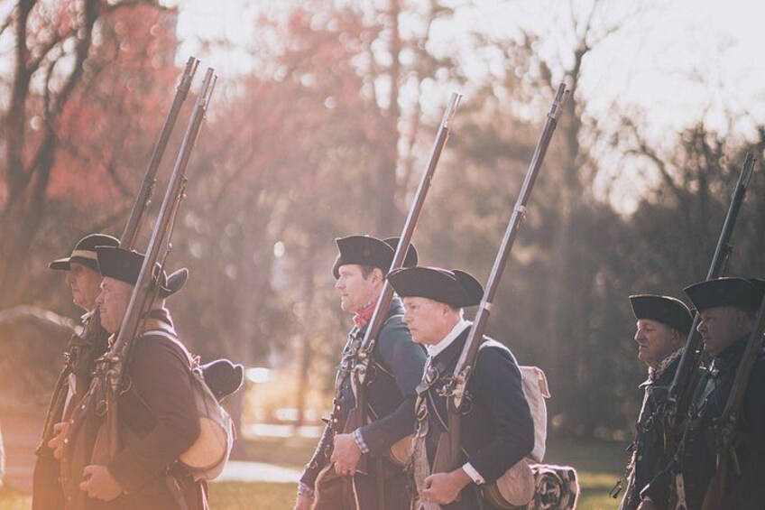 A group of people in historical military uniforms holding rifles, standing in a line outdoors. 3