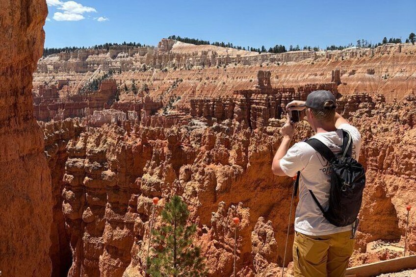 A person taking a photo of a canyon with layered rock formations. 2