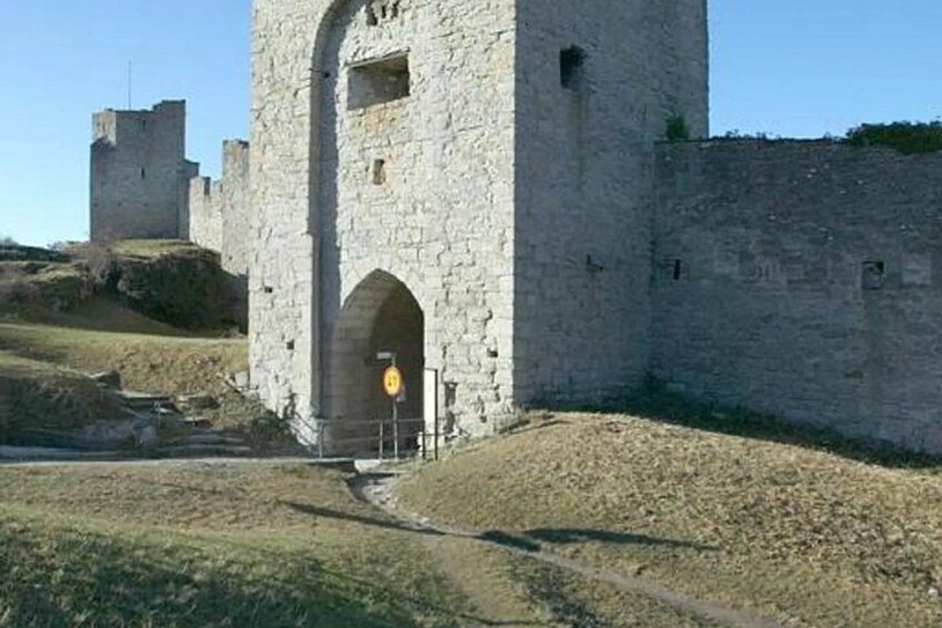 A stone tower with an arched entrance, a castle in the background, and a clear sky. 3