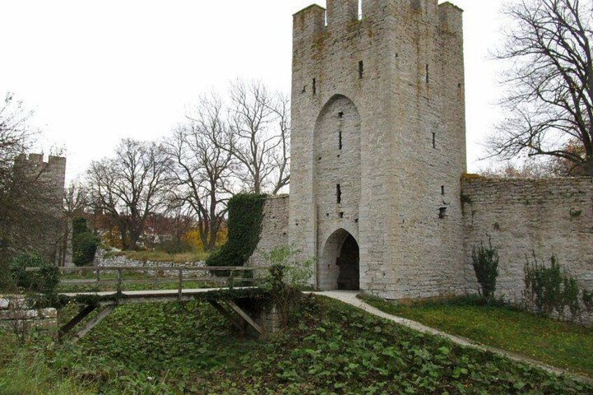 A medieval stone tower with a large arched entrance, surrounded by greenery and a stone wall. 2