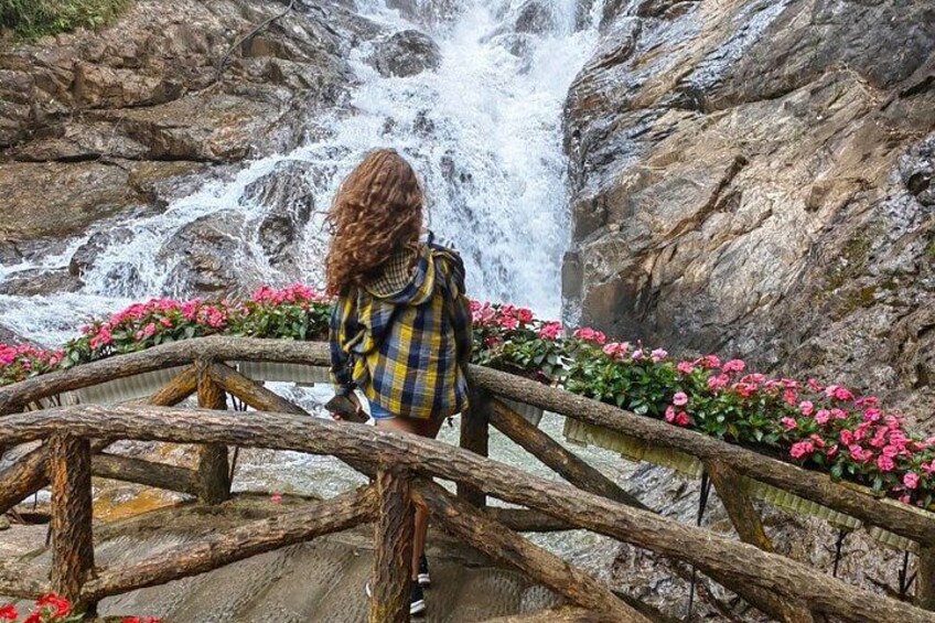 A person standing on a wooden bridge with a waterfall in the background. 4