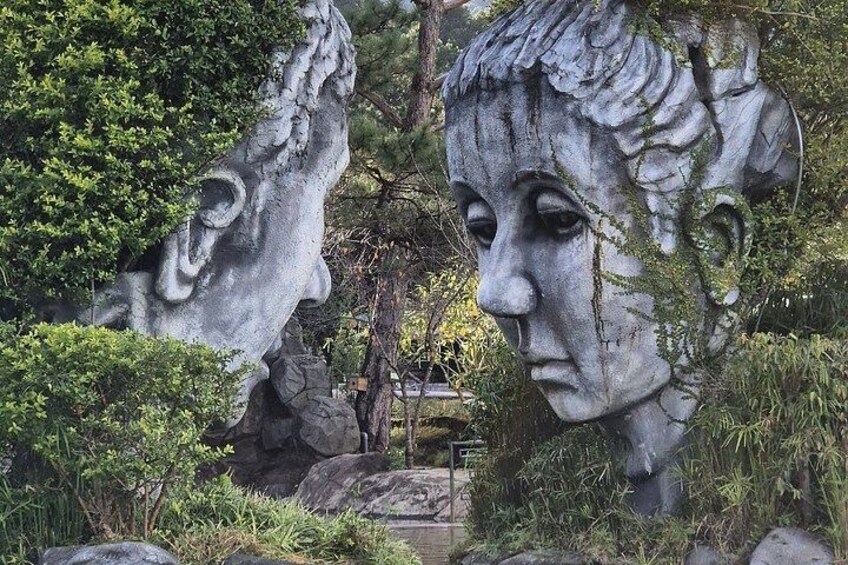 A stone sculpture of a face with foliage, set in a garden with rocks and greenery. 5