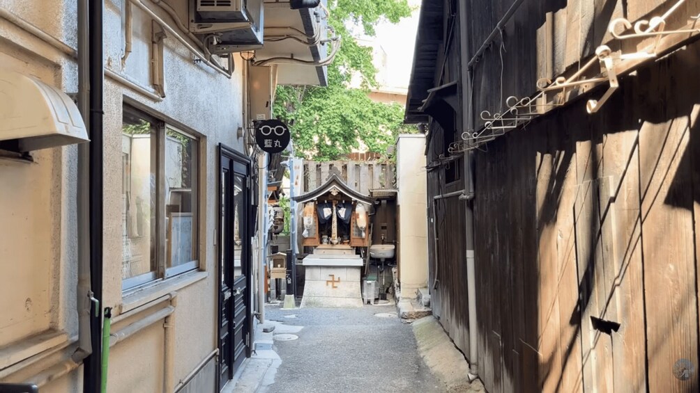 A narrow alleyway with a traditional shrine, a wooden fence, and a building with a black gate. 3