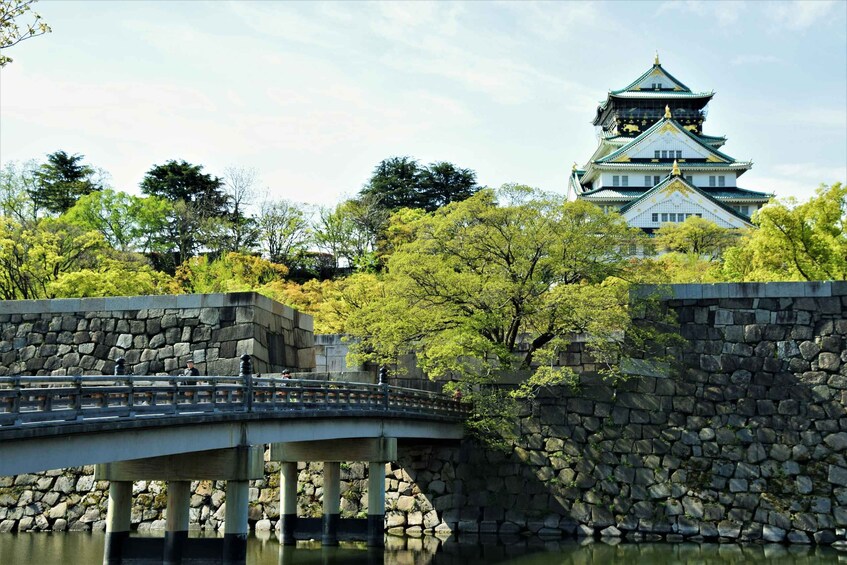 A stone bridge over water, a castle with multiple tiers, and lush green trees. 1