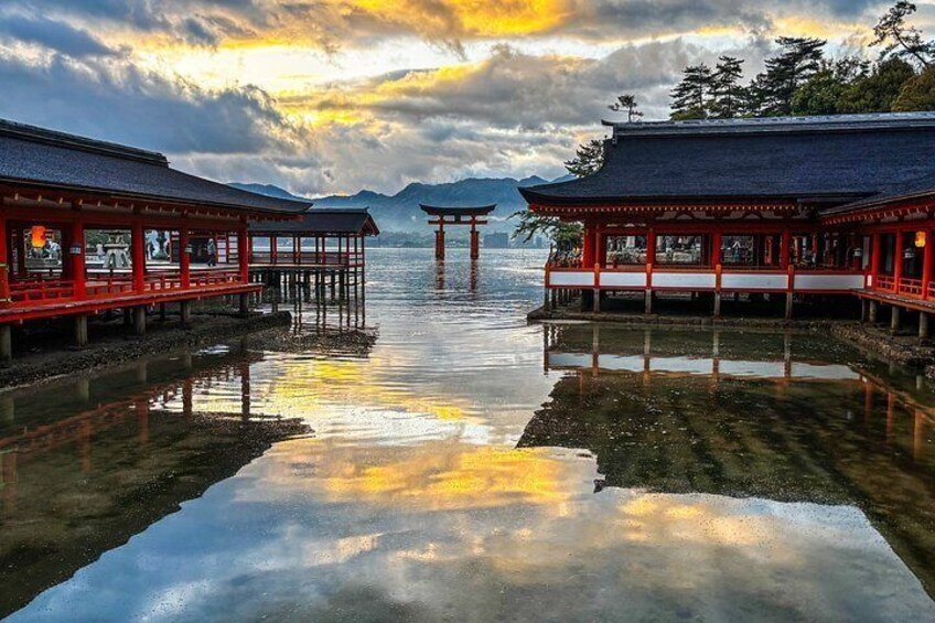 A traditional Japanese pavilion by a calm lake with reflections of the sky and distant mountains. 2