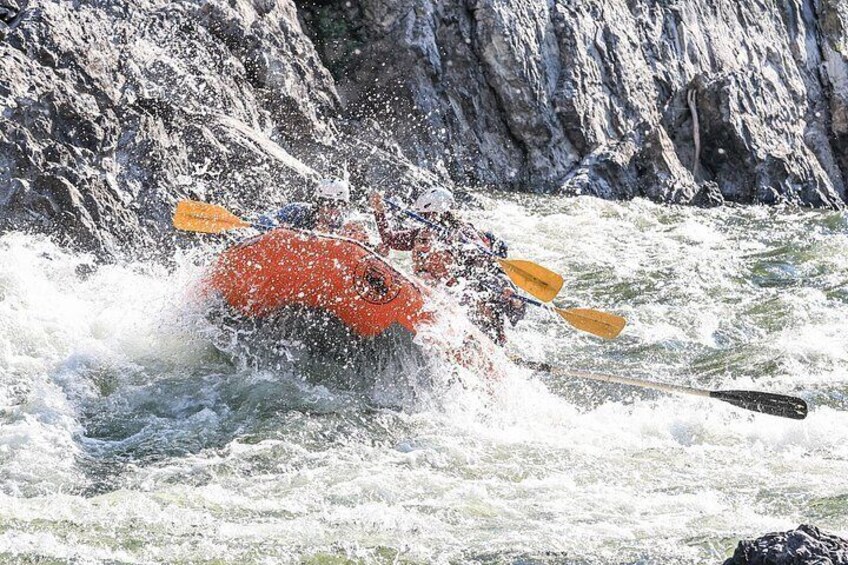 A person in a red kayak navigating turbulent waters with a rocky riverbank in the background. 3