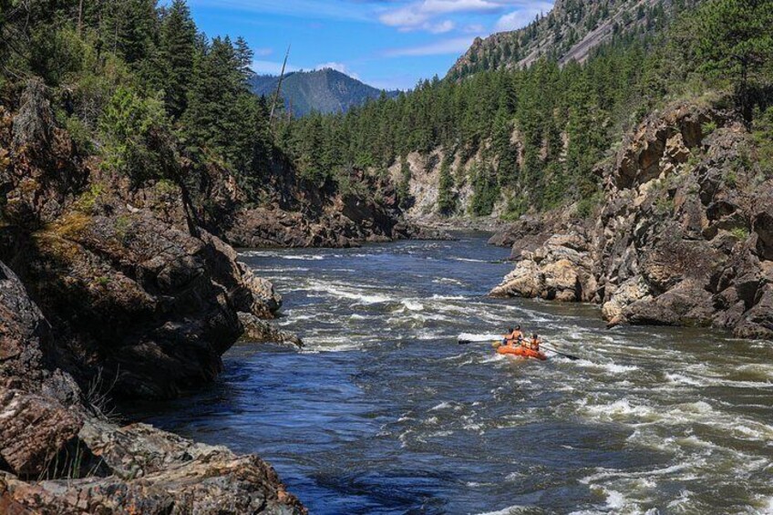 A river with a raft, surrounded by rocky cliffs and dense forest. 4