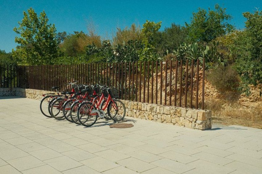 A row of red bicycles parked against a stone wall with a metal fence in the background. 4