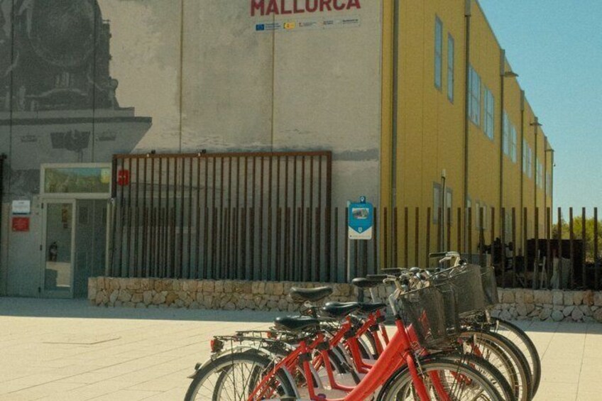 A row of bicycles parked in front of a building with a sign that reads 'MALLORCA'. 3