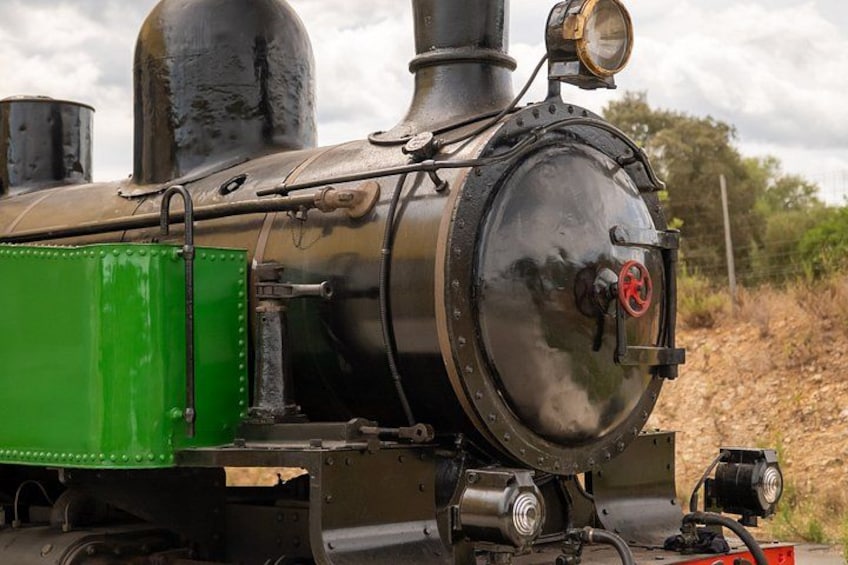 A steam locomotive with a green tender, a large smokestack, and a red signal light. 5