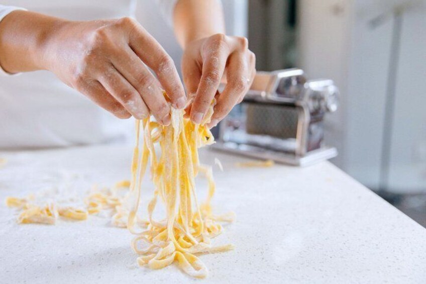 Hands peeling pasta from a machine. 1